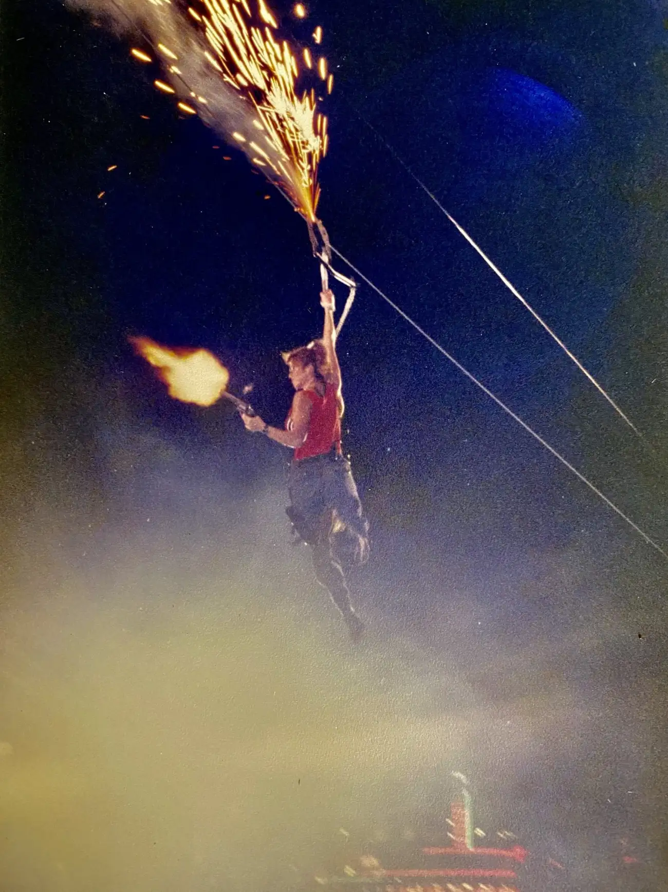 Jodi Brockton suspended on a descender rig at night, firing a live flame effect with pyrotechnic sparks streaming above her